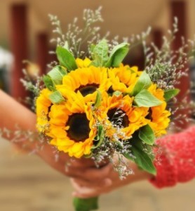 A bouquet of sunflowers, leaves and white flowers passed from one hand to another